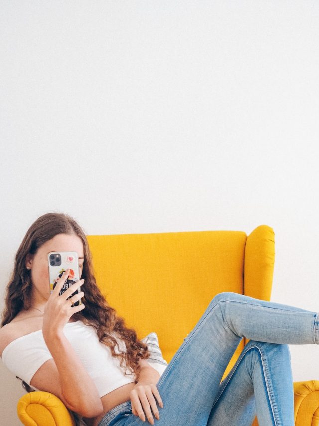 woman in white tank top and blue denim jeans sitting on yellow sofa